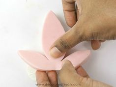 two hands are holding small pieces of pink clay that look like butterfly shaped shapes, with one hand pointing at the other