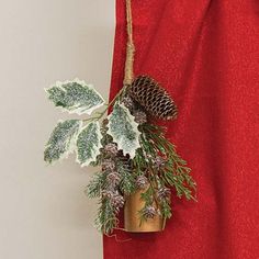 a christmas decoration hanging from the side of a red curtain with pine cones and evergreens