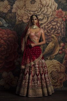 a woman in a red and gold bridal gown standing next to a floral wall