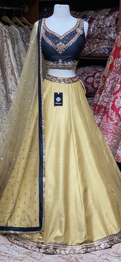 Bright gold plain skirt with black foiled work waist border paired with contrasting black kundan, stone and zardozi embroidery blouse and butti net dupatta. Fabric: Raw Silk This outfit can be customized in multiple colors and specific to client measurements. 90 days of production time is required and are for bulk orders only! Orders are processed in store only! Final fittings/alterations not included. Minimum Order Quantity- 4 pieces Designer Gold Lehenga With Mirror Work, Gold Lehenga With Mirror Work For Designer Wear, Traditional Drape Gold Sets With Mirror Work, Traditional Gold Sets With Mirror Work, Gold Bollywood Designer Lehenga, Bollywood Style Designer Gold Lehenga, Gold Raw Silk Sharara With Sheer Dupatta, Gold Designer Wear Lehenga With Traditional Drape, Gold Lehenga With Mirror Work Floor-length