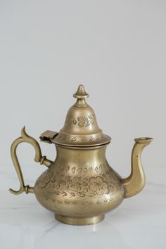 an antique brass teapot with ornate designs on the lid and handle is shown against a white background