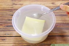 a person is holding a spoon over a container of yogurt and butter on a wooden table