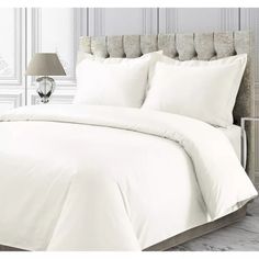 a bed with white sheets and pillows on top of it in a room next to a lamp