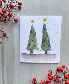 a card with two christmas trees on it next to some red berries and greenery