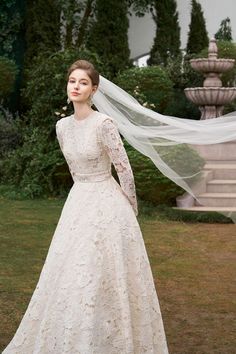 a woman in a white wedding dress with a veil over her head standing on the grass