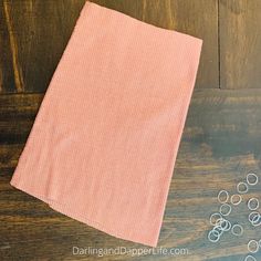 a pink towel sitting on top of a wooden table next to some scissors and beads