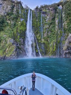 a man standing on the bow of a boat in front of a waterfall