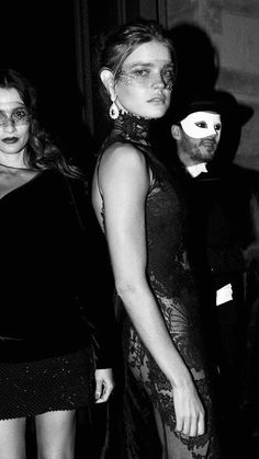 two women in black dresses standing next to each other with white masks on their faces