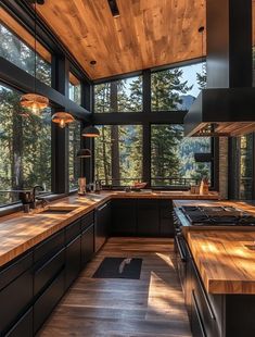 a large kitchen with wooden counters and floor to ceiling windows that overlook the trees outside