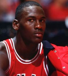 a young man in a red jersey sitting on the sidelines at a basketball game