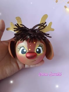 a hand holding a small doll with hair on it's head and eyes painted to look like a reindeer