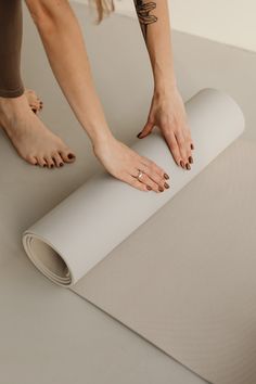 a woman rolling up a yoga mat on top of the floor with her hands resting on it