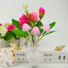 a white vase filled with pink flowers and seashells