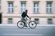 the man is riding his bike down the street in front of a building with many windows