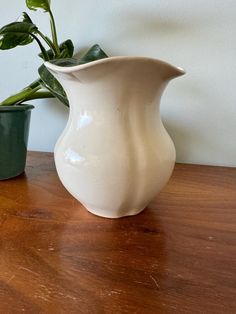 a white vase sitting on top of a wooden table next to two small green pots