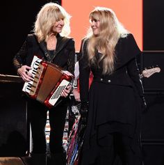 two women standing next to each other holding an accordion