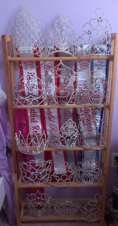 a wooden shelf filled with lots of crowns and tiaras on top of each other