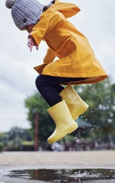 a person jumping in the air wearing rain boots and a yellow coat with a hat on