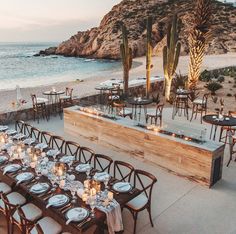 an outdoor dining area with tables and chairs on the beach next to the ocean at dusk