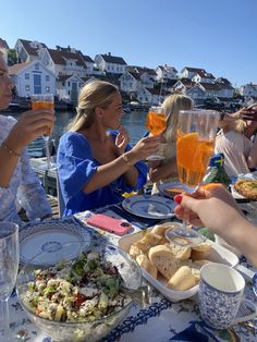 people sitting at a table with food and drinks in front of them, overlooking the water