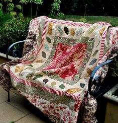 a quilted couch sitting on top of a metal bench in front of some bushes