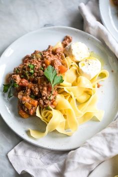 a white plate topped with pasta covered in meat and sauce next to another plate filled with eggs