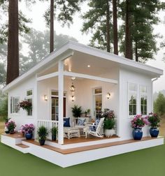 a small white house in the woods with flowers on the porch and potted plants