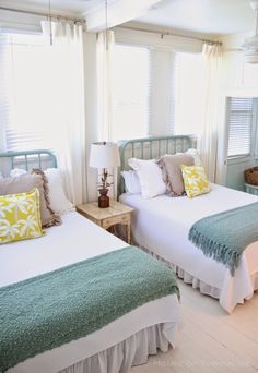 two beds in a room with white walls and green bedding, one has yellow pillows on it