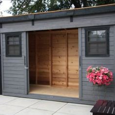 a wooden shed with its doors open and flowers in the potted planter next to it