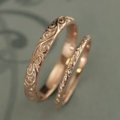 two gold wedding bands on top of each other, one with an intricate design in the middle