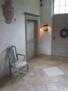 a chair sitting in the corner of a room with a door and wreath on the wall