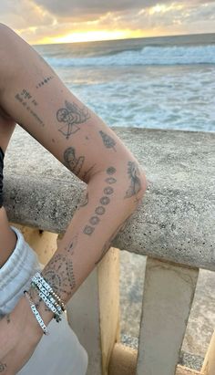 a woman with tattoos on her arm leaning against a railing near the ocean at sunset