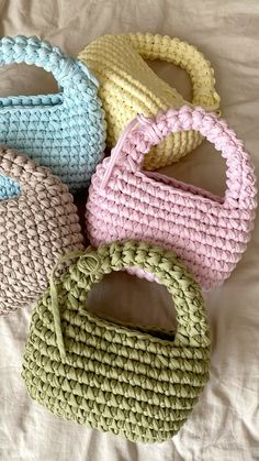 four crocheted purses sitting on top of a white bed next to each other