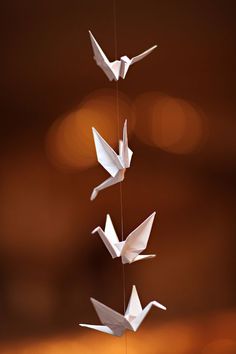 three white origami birds hanging from strings in front of a blurry background