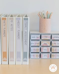 the books are lined up next to each other on the desk with pens and pencils in them