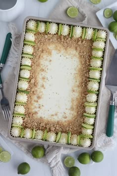 a square cake with limes around it on a white table cloth next to utensils