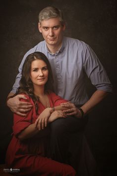 a man and woman are posing for a photo in front of a dark background with their arms around each other