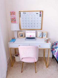 a white desk topped with a laptop computer and a pink chair next to a wall mounted calendar