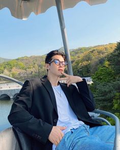 a man sitting on top of a boat next to a river under an open umbrella