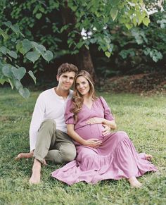 a pregnant couple sitting in the grass under a tree