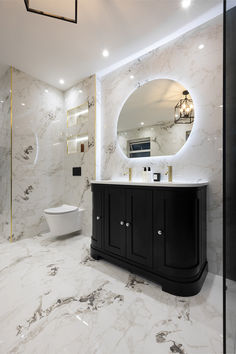 a bathroom with marble walls and flooring has a round mirror above the vanity, along with a white toilet