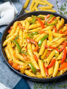 a bowl filled with pasta and peppers on top of a blue table cloth next to some cut up vegetables