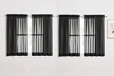 two black sheer curtains hanging on the side of a white wall next to a window