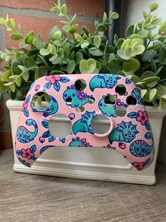 a pink and blue nintendo wii controller case sitting on top of a wooden table next to a potted plant