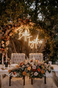 a table with flowers and chairs under a neon sign that says better together on it