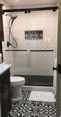 a white toilet sitting next to a walk in shower under a black and white tiled floor