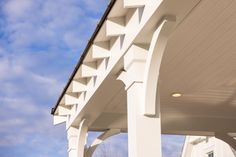 the side of a white house with an awning on it's roof and blue sky in the background