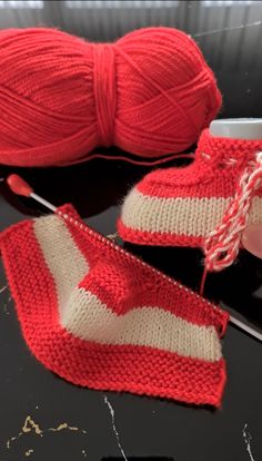 a pair of red and white knitted shoes next to a ball of yarn