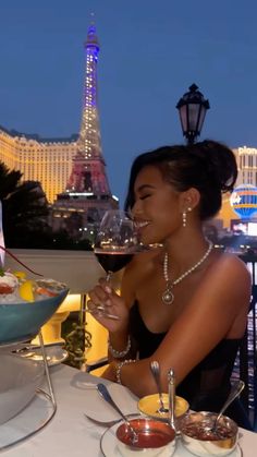 a woman sitting at a table with a glass of wine in front of the eiffel tower