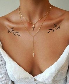 a woman with tattoos on her chest wearing a white top and gold chain choker